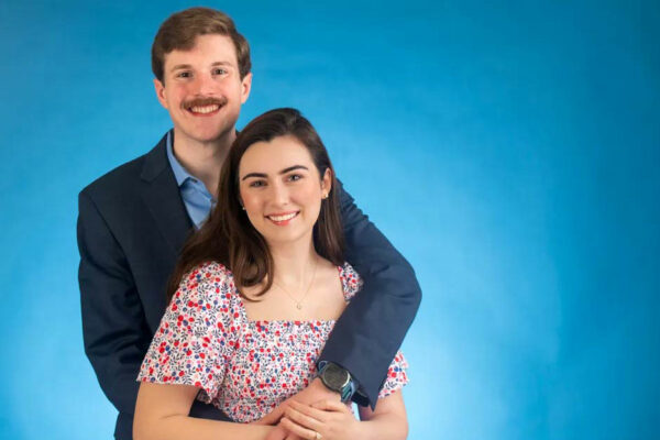 A Young Couple With Arms Around Each Other Pose For A Photo