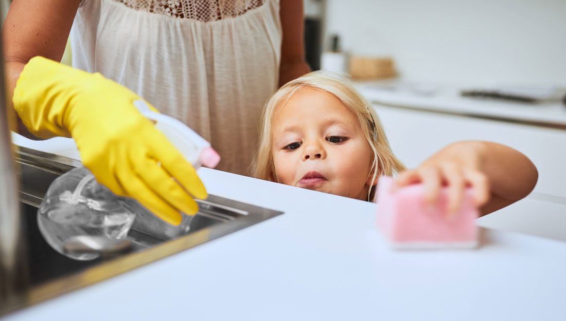 a mother and her little daughter cleaning a kitchen surface together at home