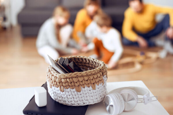 Family Plays Game Together In Background While Phones Sit In A Basket In Foreground