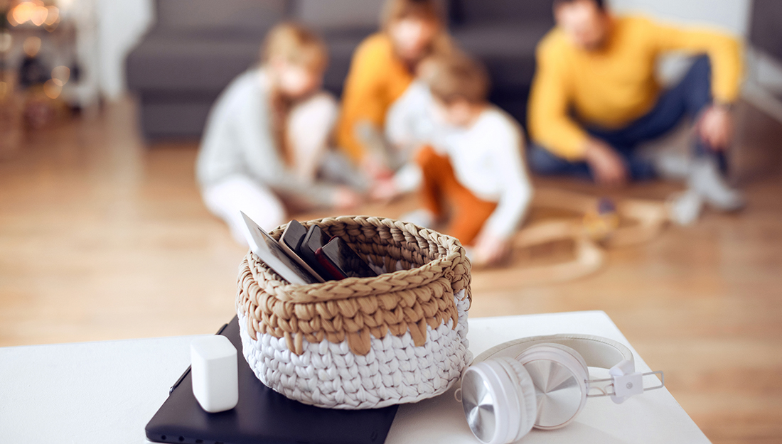 Family plays game together in background while phones sit in a basket in foreground