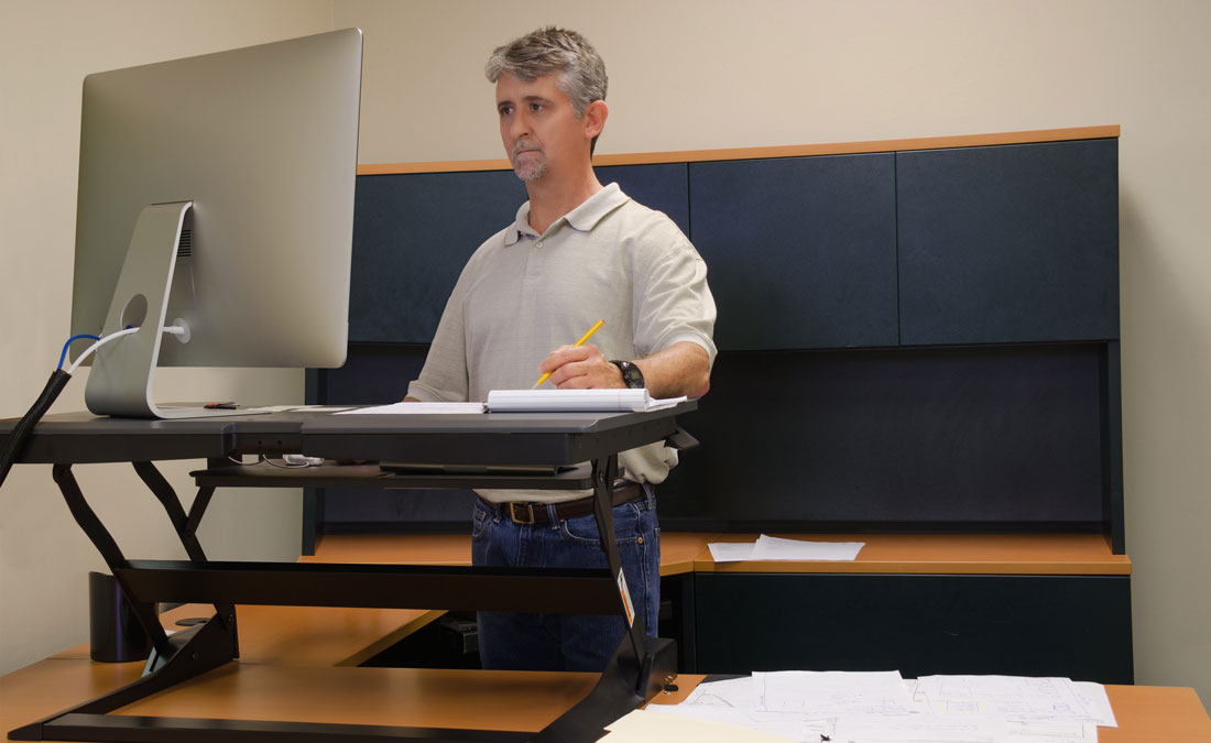 man works on computer at a standing desk workstation