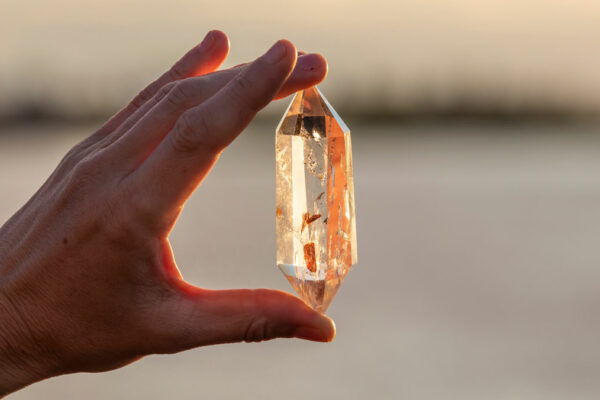 A Hand Holding Up A Beautiful Quartz Crystal Outdoors In The Sun