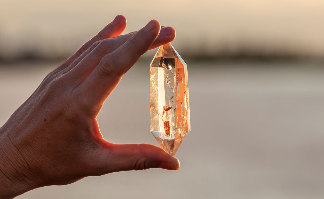 A hand holding up a beautiful quartz crystal outdoors in the sun