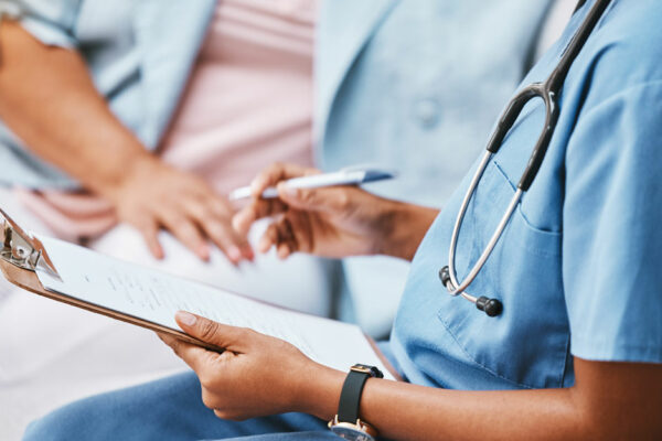 Health Care Professional Holds A Clipboard, Sits Beside A Patient, Discusses Health Care Plan And Prior Authorization