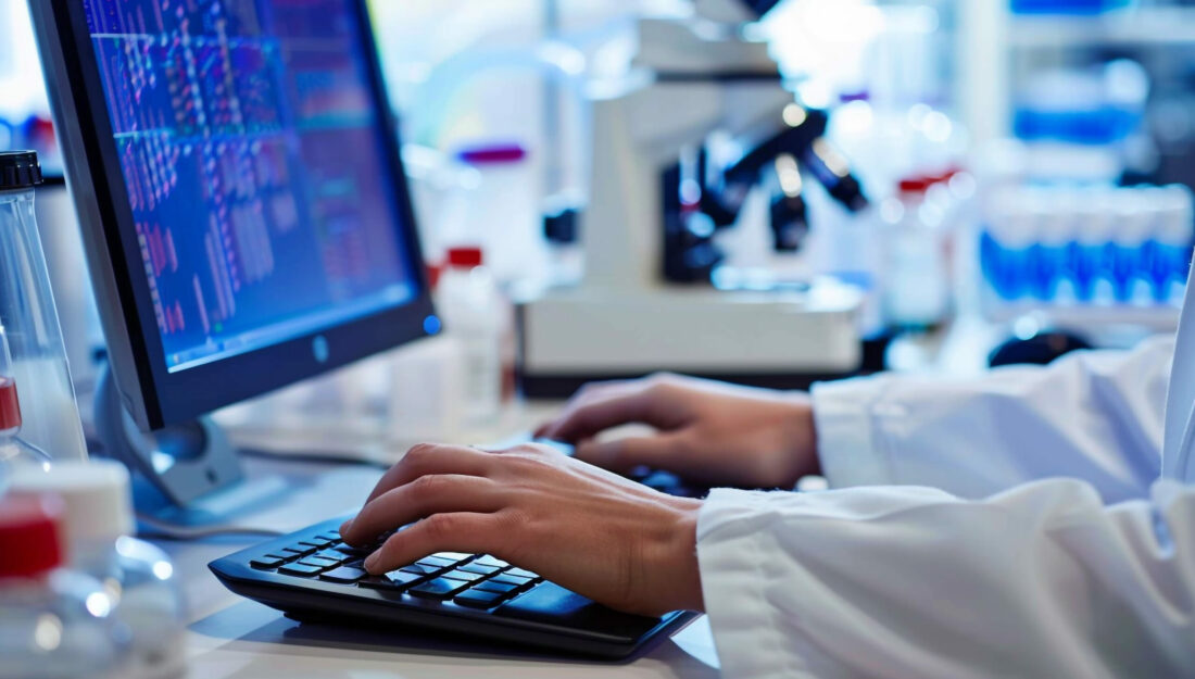 person wearing a white coat types on a keyboard with medical research software open