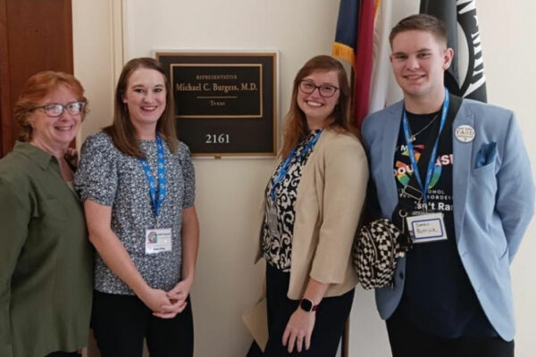 Four People In Business Attire Stand Together In Front An Office Sign That Says "Representative Michael C. Burgess, MD, Texas"