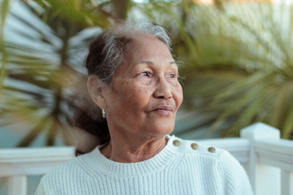 Senior Filipino Woman Sitting In Her Garden, Surrounded By Palm Trees