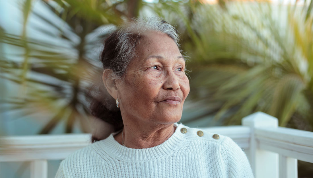 senior filipino woman sitting in her garden, surrounded by palm trees