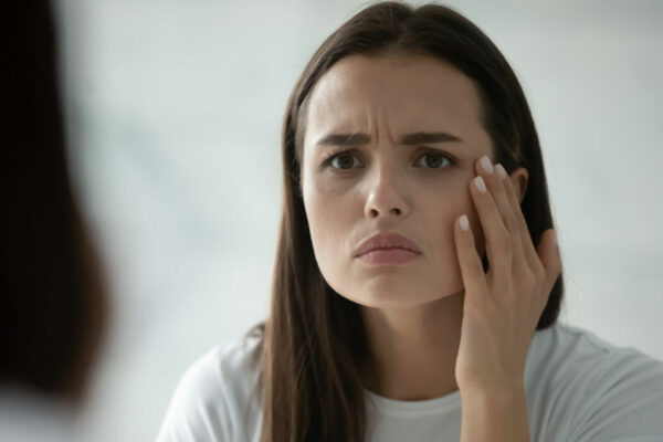 Unhappy Young Woman Wearing A White T-shirt Looks In The Mirror