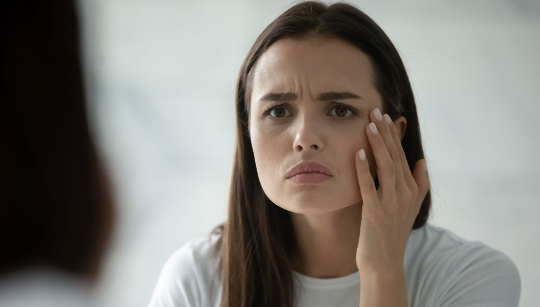 unhappy young woman wearing a white t-shirt looks in the mirror