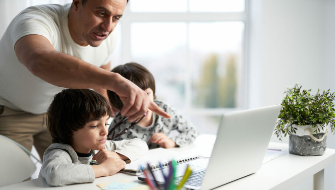 father helps his two young children work on a computer