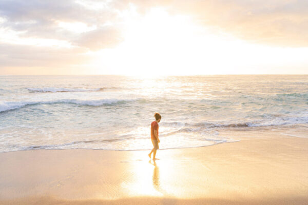 Young Man Walking Alone On The Beach On A Summer Day With Beautiful Sunset Light