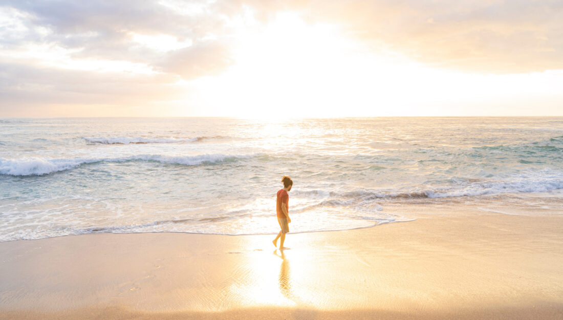 Young man walking alone on the beach on a summer day with beautiful sunset light