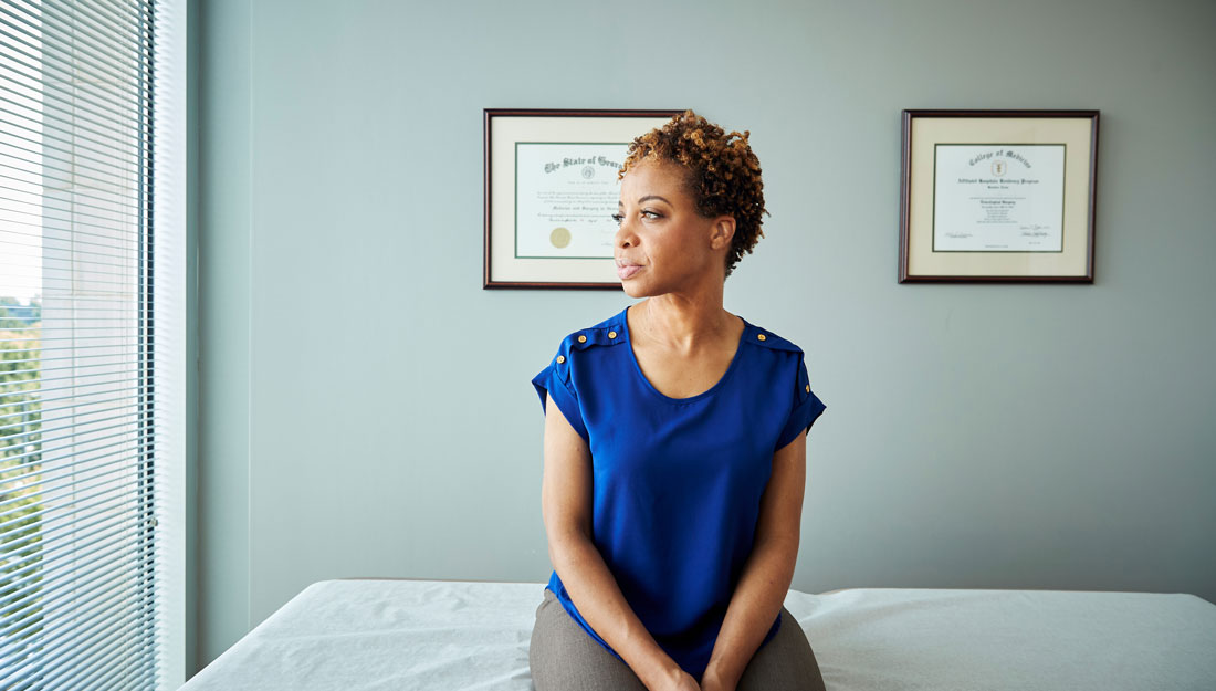 woman sits on an exam room table in a doctor's office, looking out the window