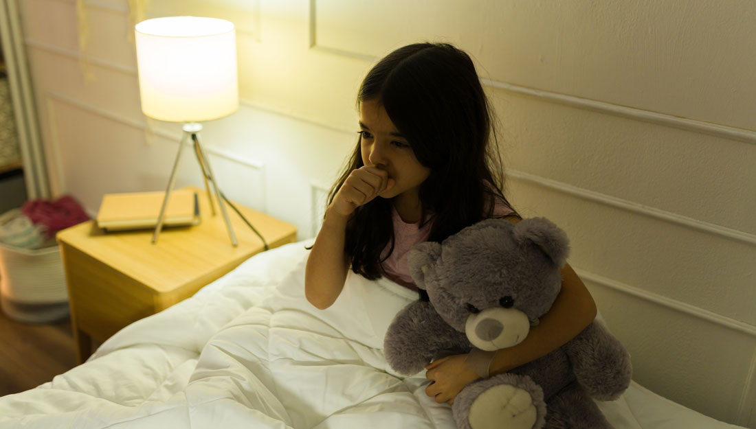 girl with her teddy bear, coughing while trying to sleep in her bedroom at night