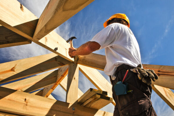 Construction Worker Wearing A Hard Hat Hammers Nails Into Boards On A Construction Projects