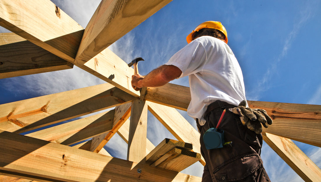 construction worker wearing a hard hat hammers nails into boards on a construction projects