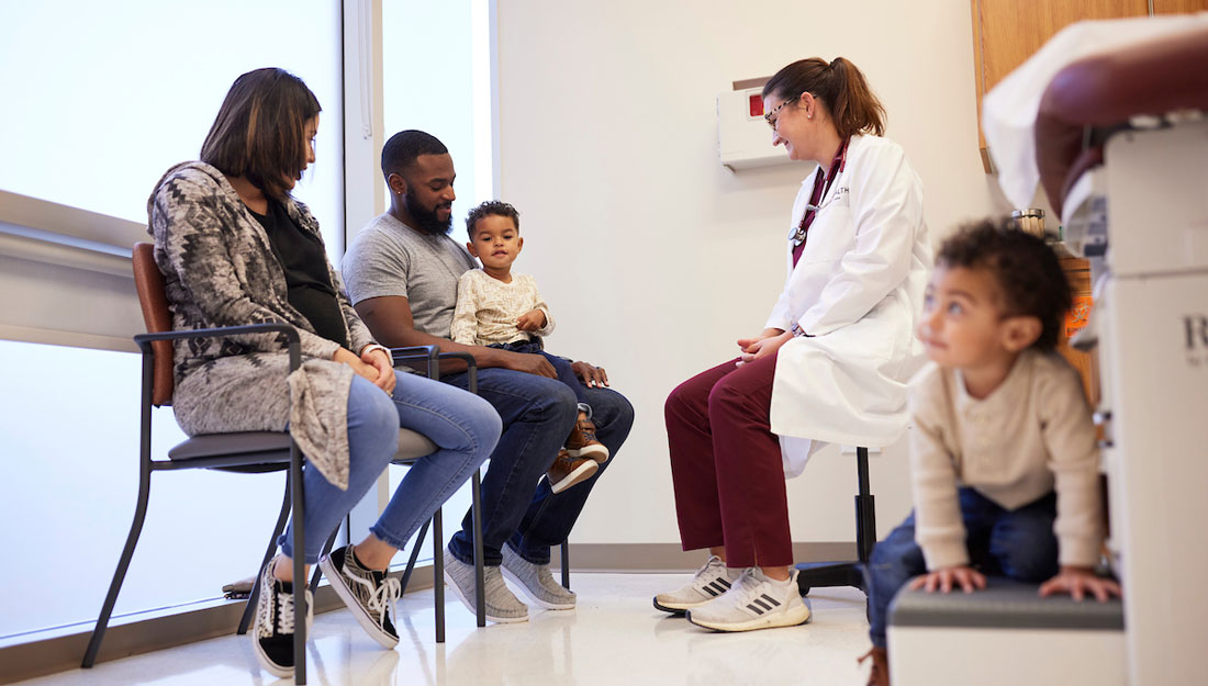 Mother, father and two toddler sons visit with a Texas A&M physician inside a clinic exam room