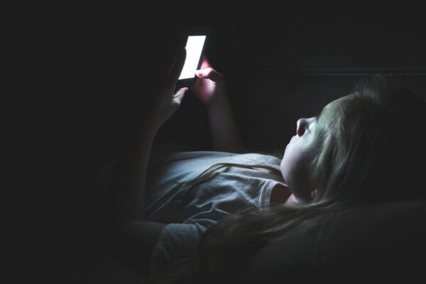 Girl Lays In Bed In The Dark While Looking At A Cell Phone Screen