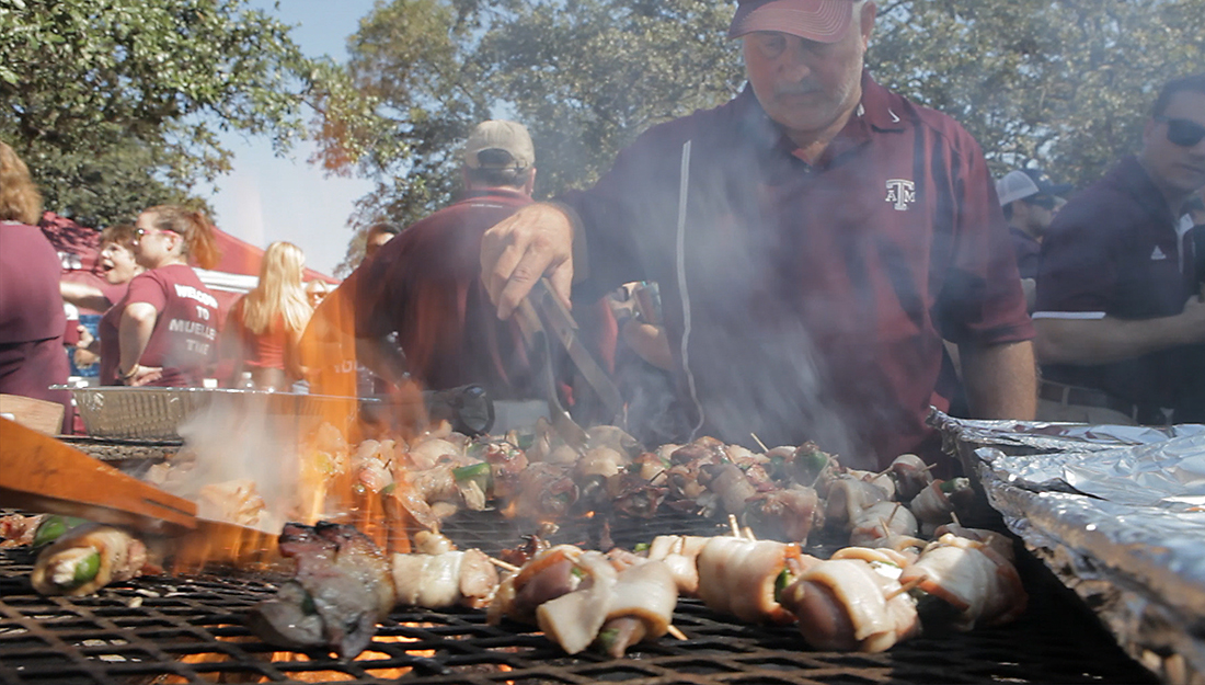 Man stands over grill flipping skewer with tongs, demonstrating tailgate safety