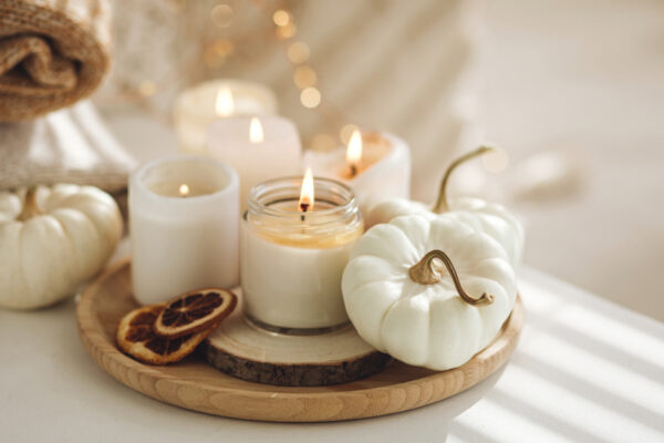 Candles Burn On A Wooden Tray That Also Holds Small Pumpkins, String Lights Glow In The Background