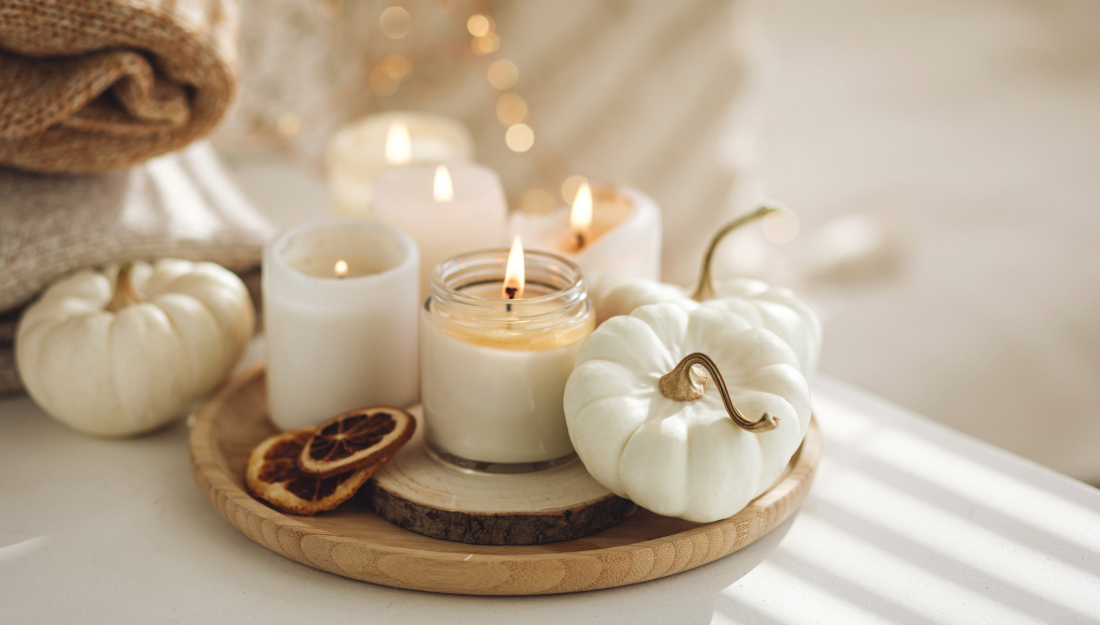 candles burn on a wooden tray that also holds small pumpkins, string lights glow in the background