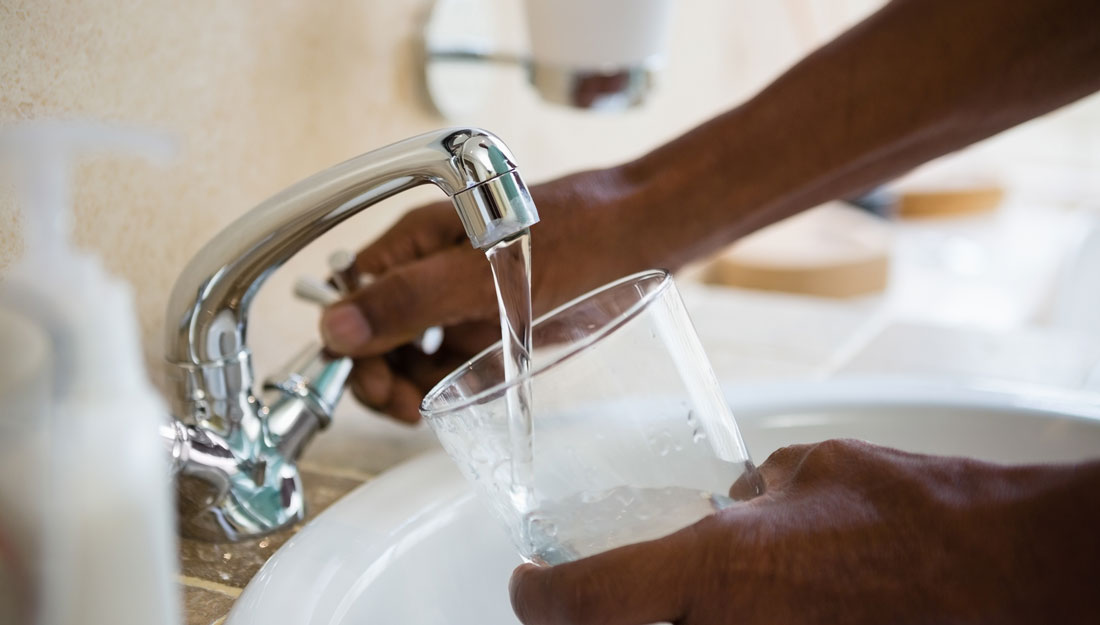 person fills a drinking glass with water from a faucet