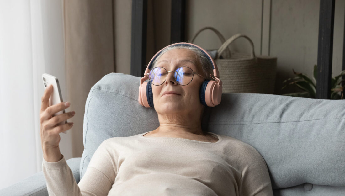 Calm senior lady in wireless headphones listening to relaxing music