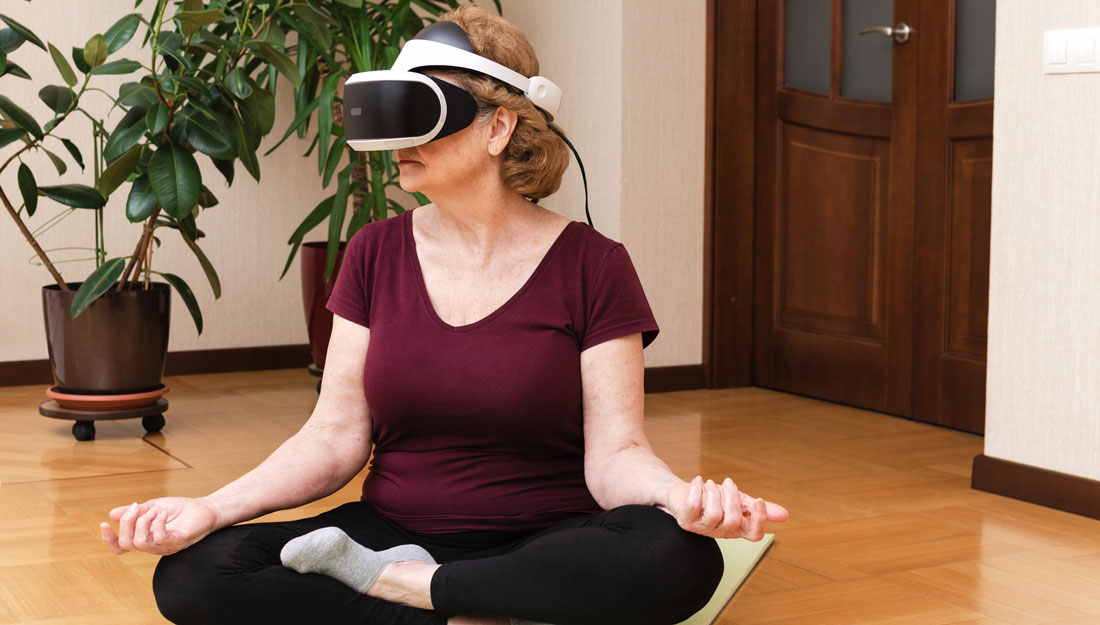 Senior woman sitting on yoga mat meditating in VR glasses at home. Virtual reality meditation