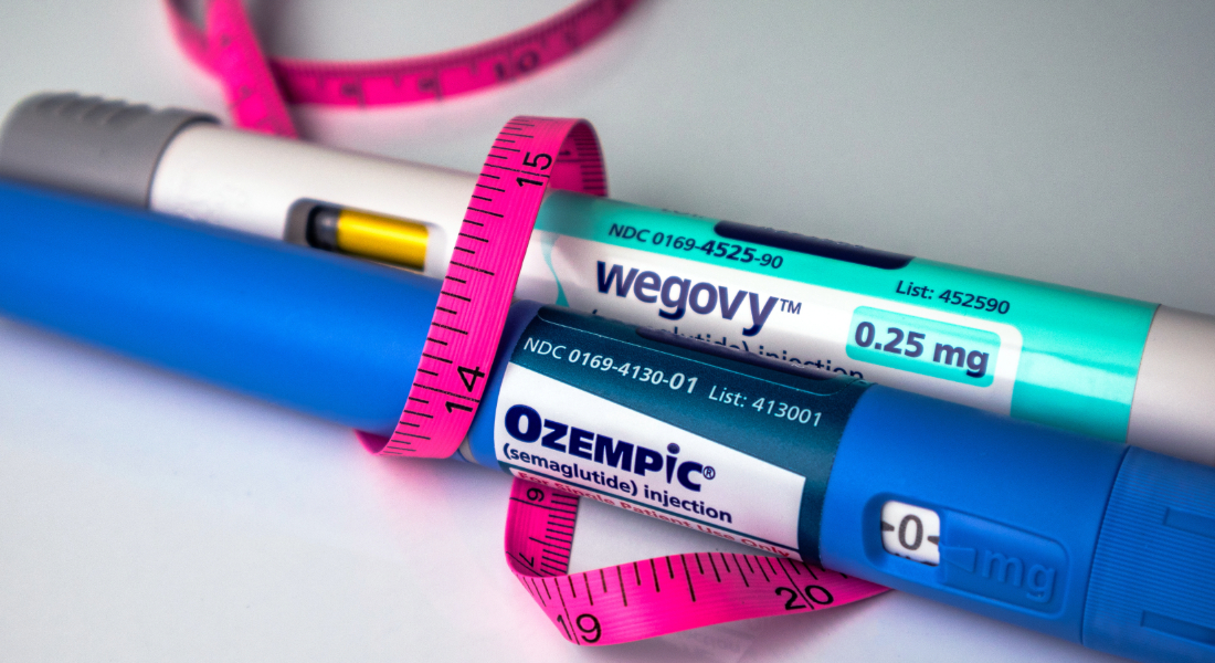 A hot pink tape measure wrapped around an Ozempic and Wegovy pen laying on a table