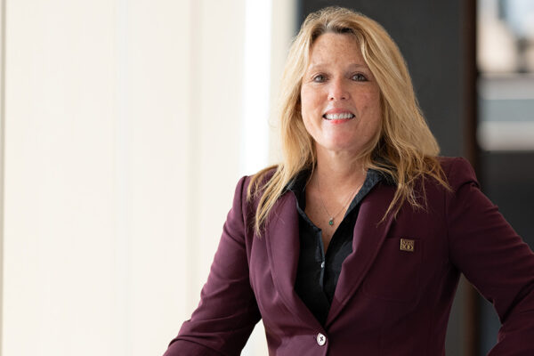 Portrait Of Jenny Hanlon, A Smiling Blonde Woman In Maroon Jacket.