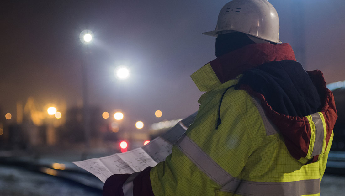 Back view of young construction worker in helmet at night reading construction drawings