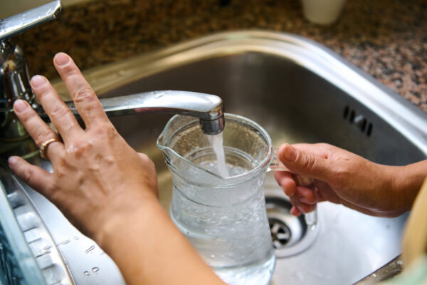 Person Filling A Glass Pitcher With Water At The Kitchen Sink