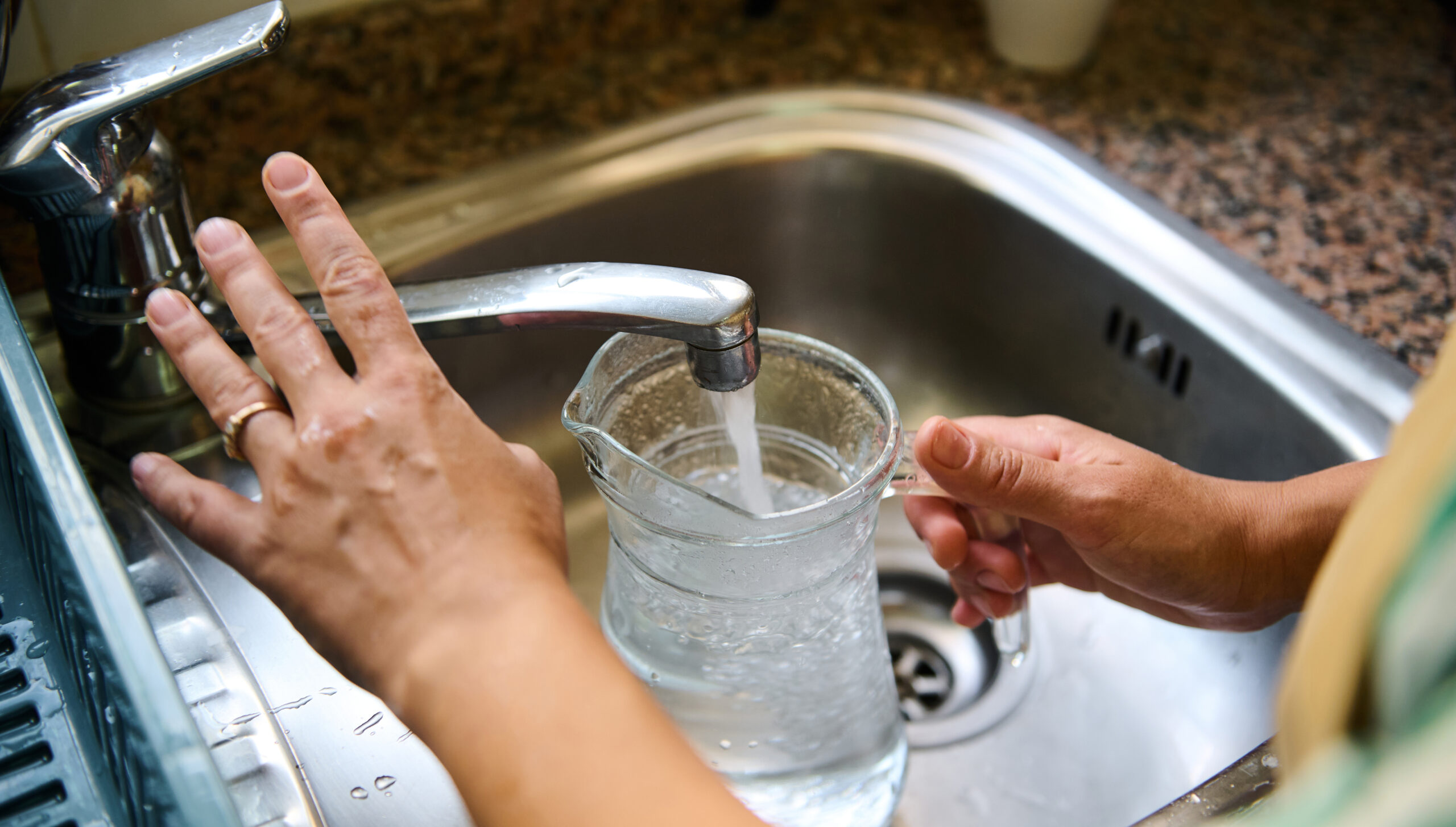 Person filling a glass pitcher with water at the kitchen sink