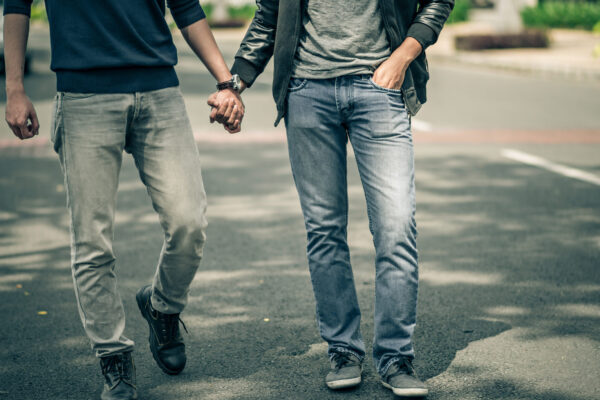 Two Men Hold Hands While Walking Down A Street