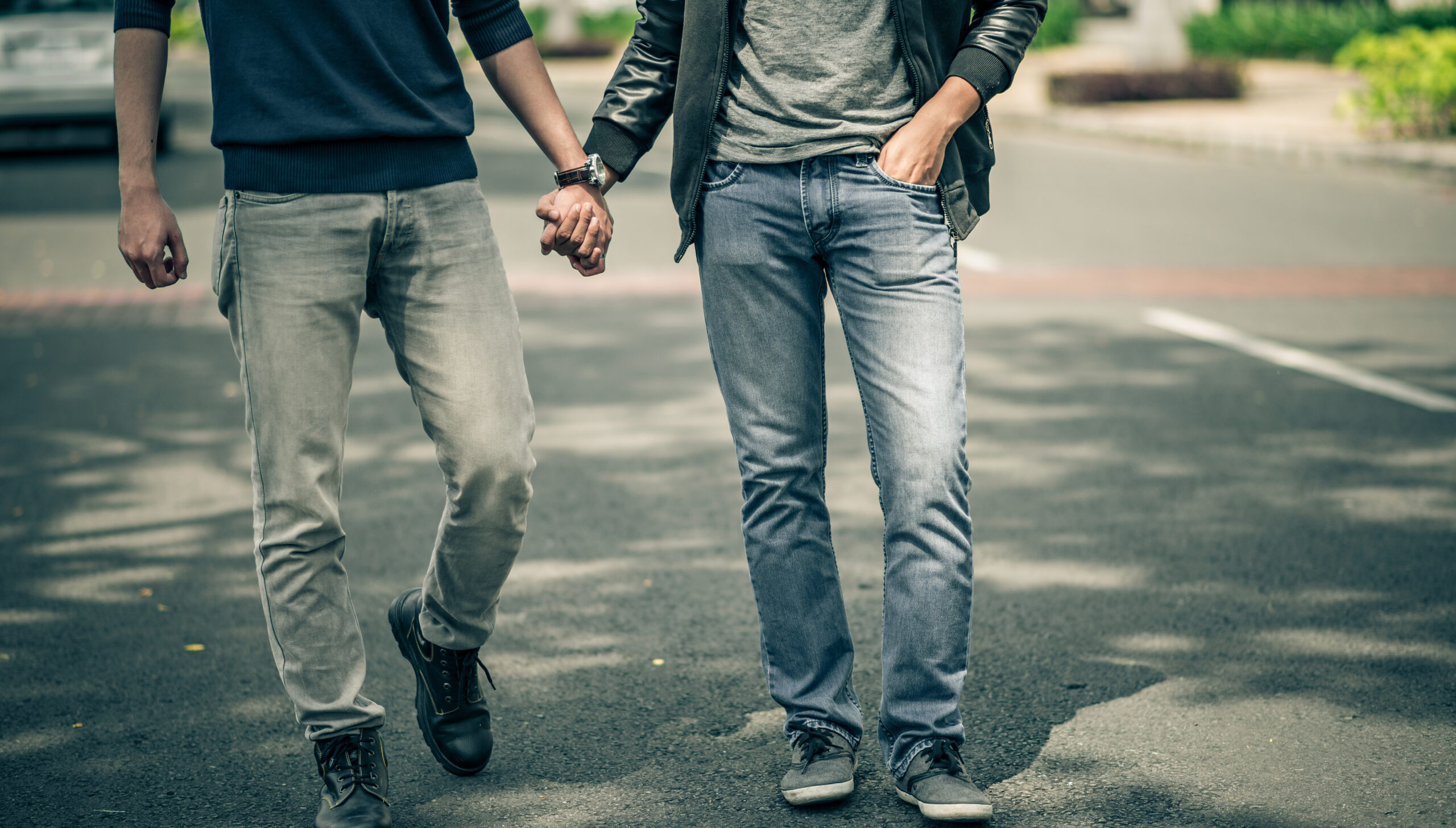 two men hold hands while walking down a street