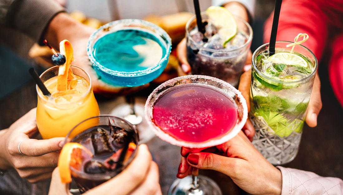 People's hands toasting multicolored fancy cocktails