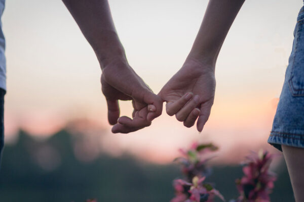 Couple Locks Pinkies While Walking Through A Meadow