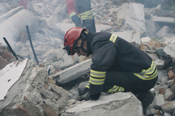 Left View Of Male Emergency Workers Removing Concrete Rubble In Cloud Of Dust While Working On Ruins Of Destroyed Building After Disaster