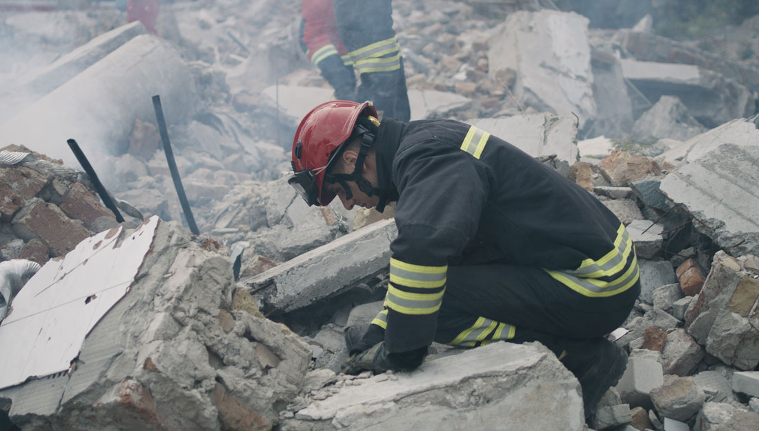 left view of male emergency workers removing concrete rubble in cloud of dust while working on ruins of destroyed building after disaster