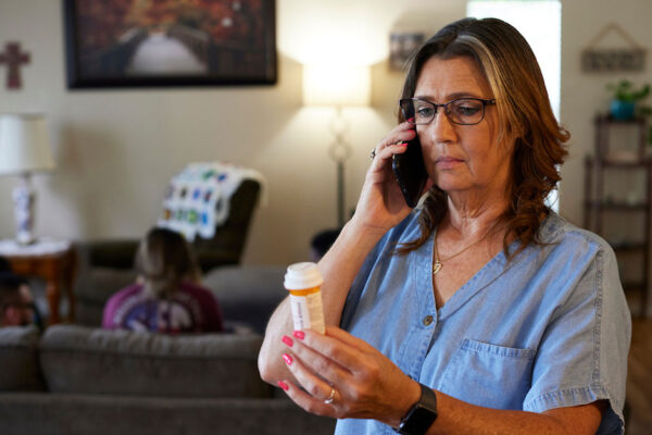 older woman talks on the phone while looking at a prescription bottle