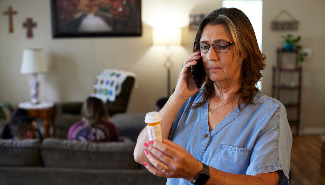 older woman talks on the phone while looking at a prescription bottle