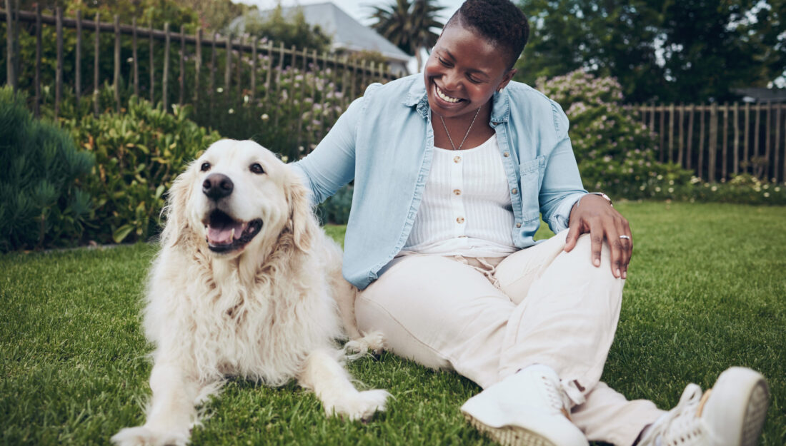 woman sits in the grass next her dog, petting it affectionately