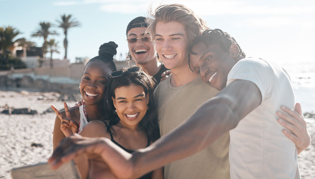 group of young adults stand together for a selfie on the beach