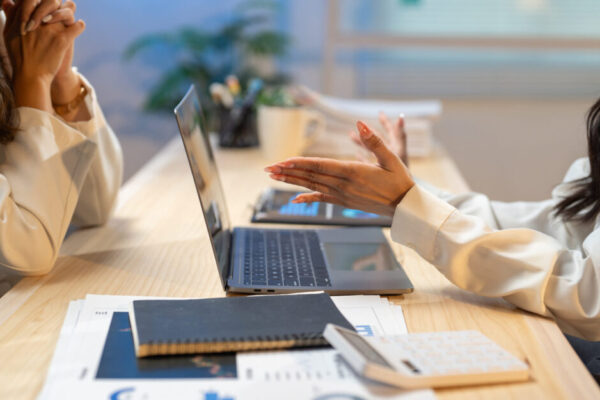 Two Businesswomen Having A Discussion Using A Laptop And Financial Reports In A Modern Office