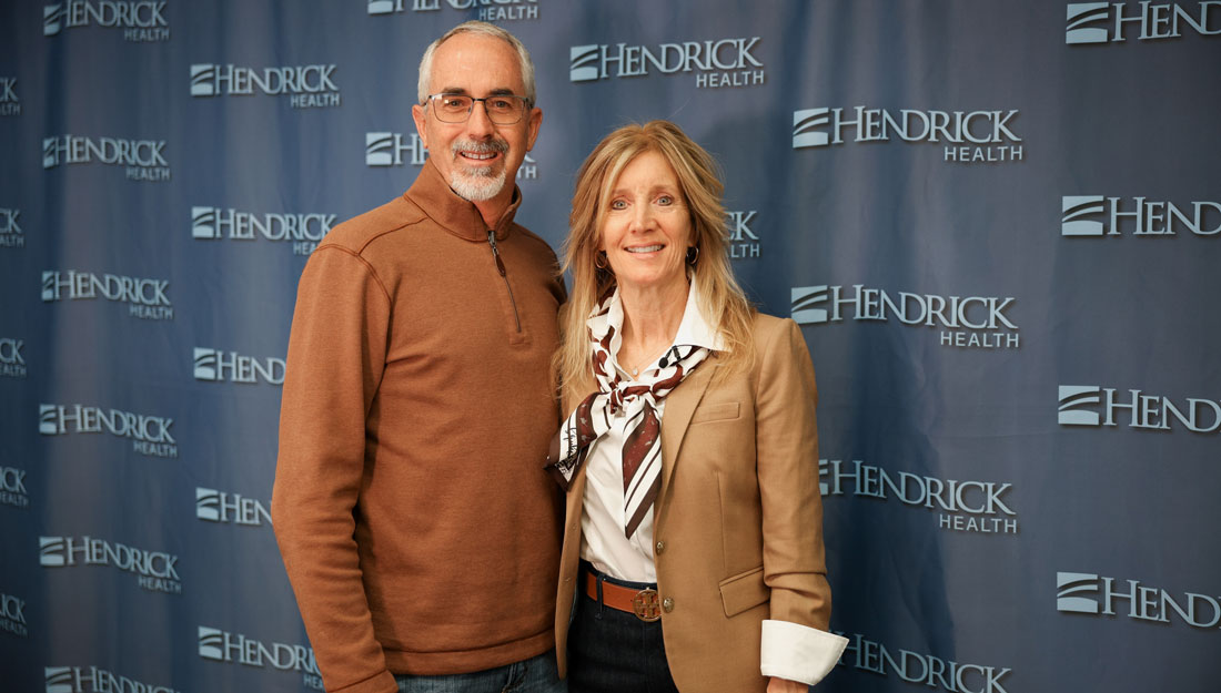 David and Wendy Grooms pose together for a photo in front of a backdrop with the Hendrick Health logo